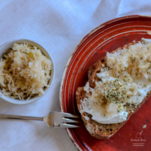 Eine Schüssel mit Sauerkraut und eine Scheibe Brot belegt mit Frischkäse, Sauerkraut und frischen Kräutern
